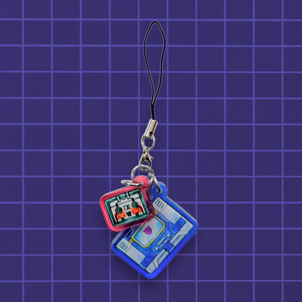 Godliath G1 Alt Mode acrylic phone charms featuring blue and red retro cassette player designs on a purple grid