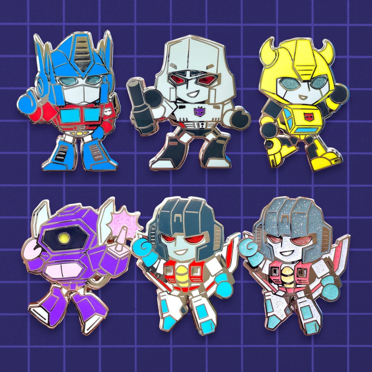 Six Transformers-themed enamel pins arranged in two rows on a purple grid background. Includes Optimus Prime, Megatron, Bumblebee, Shockwave, Starscream, and Ghost Starscream with glitter enamel.
