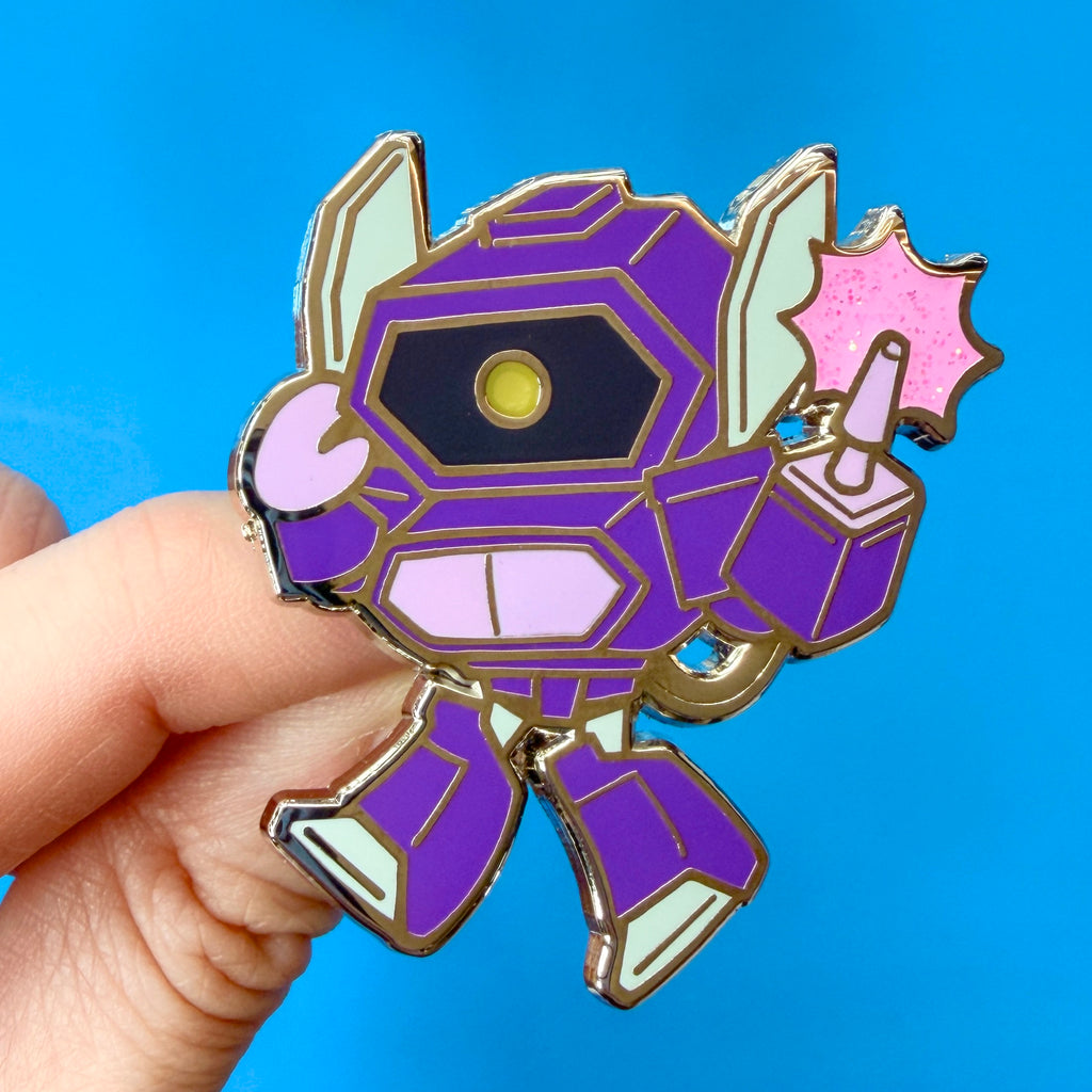A close-up of a hand holding a chibi Transformers Shockwave enamel pin